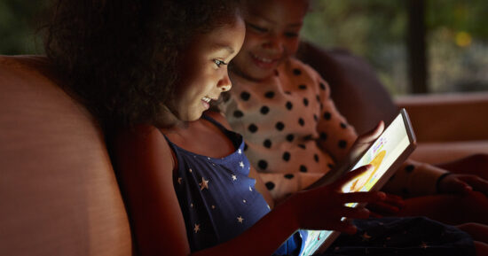 Two young girls playing on digital tablet, at night